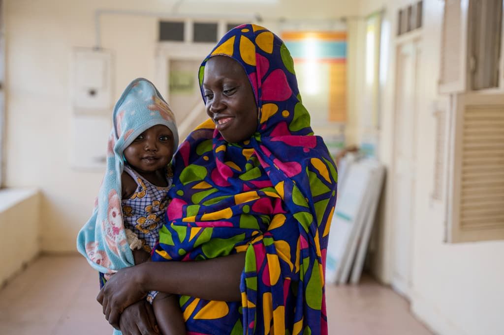 A mother holds her baby daughter at a healthcare centre supported by Islamic Relief in Gedaref, Sudan, after the child recovered from severe acute malnutrition.