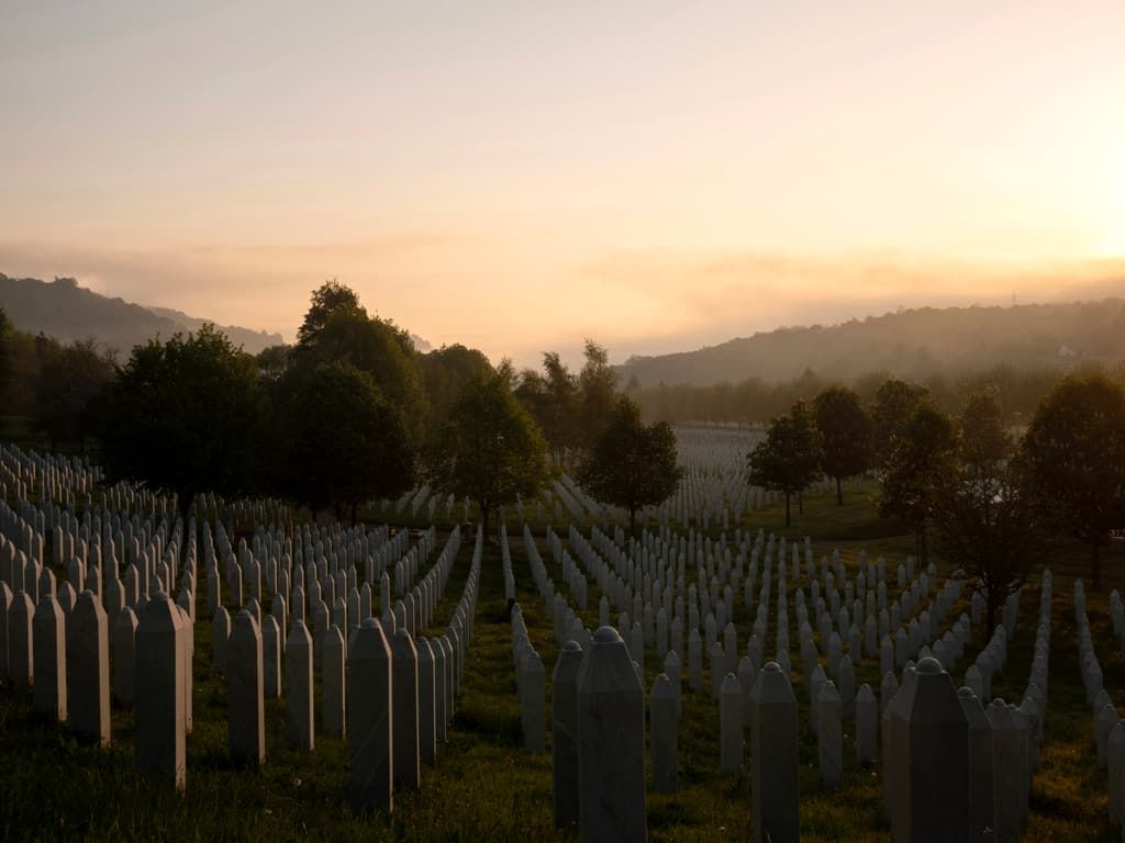 Rows of white grave markers at the Srebrenica–Potočari memorial cemetery at dawn.