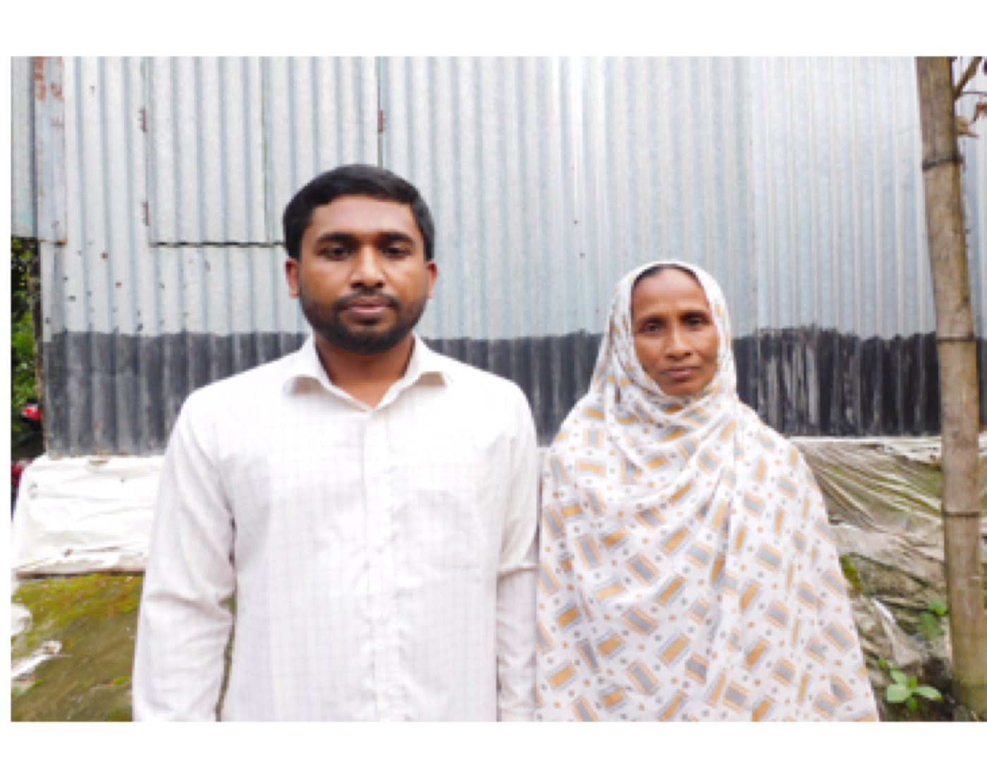 Milon stands beside his mother outside their home in Bangladesh.