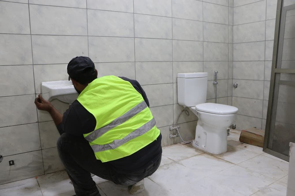 A worker in a high-visibility vest fits wall tiles in a newly refurbished hospital bathroom in Lebanon.