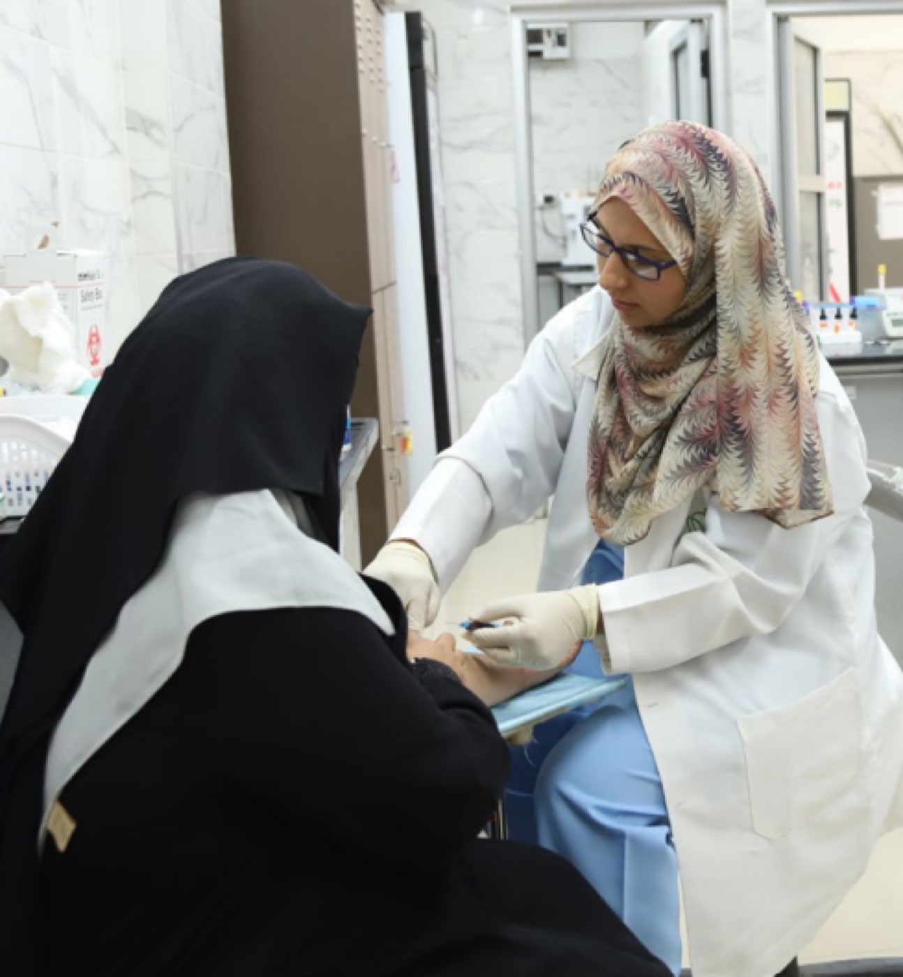 A female health worker in a white coat treats a patient at a clinic.